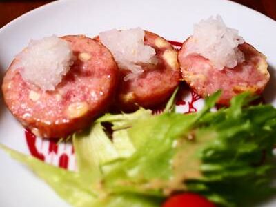 焼いたチーズリオナソーセージに大根おろしをトッピングした一皿。フリルレタスとミニトマトが添えられている。